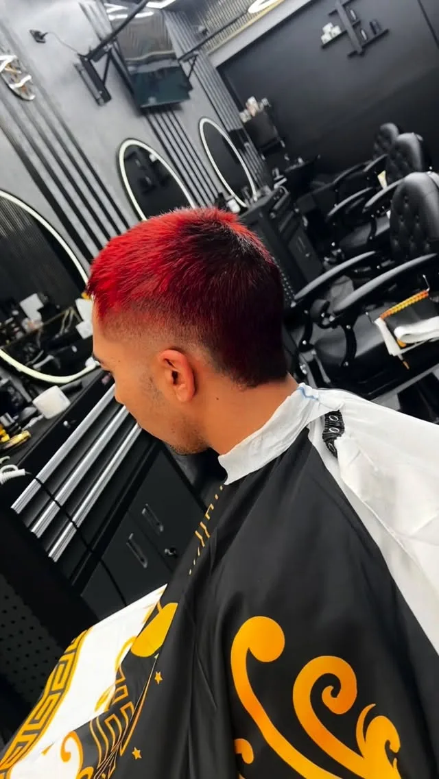 Bold red-dyed crop and skin fade, black and gold swirl cape, ring mirrors — colour service.