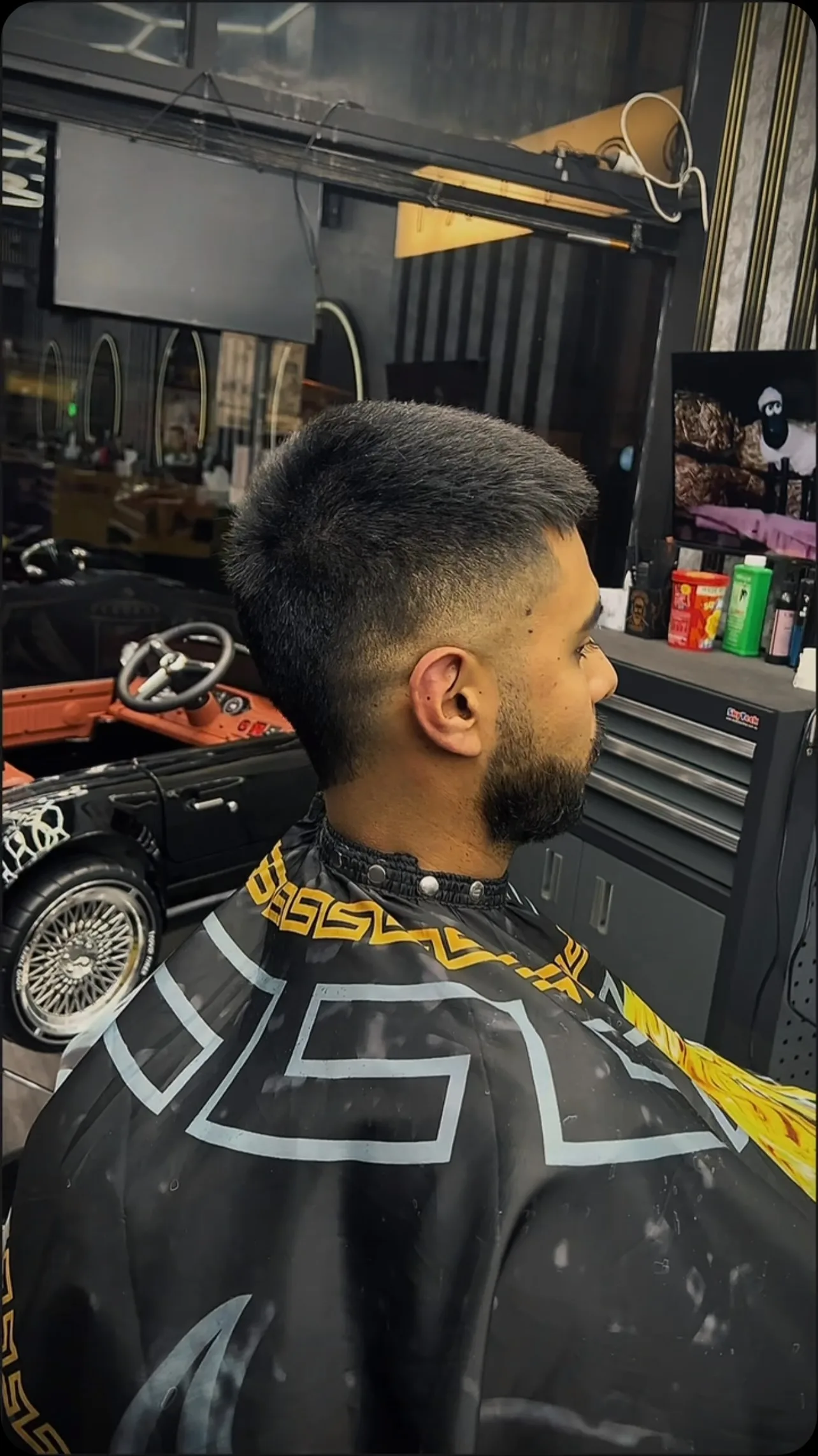 Side profile, slicked-back longer top and taper, full beard, pinstripe cape.