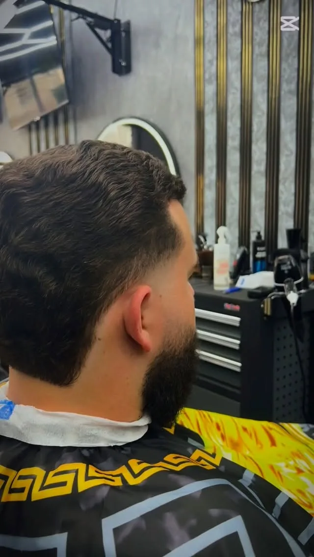 Wavy hair mid-taper with full beard, Versace cape, gold slat wall