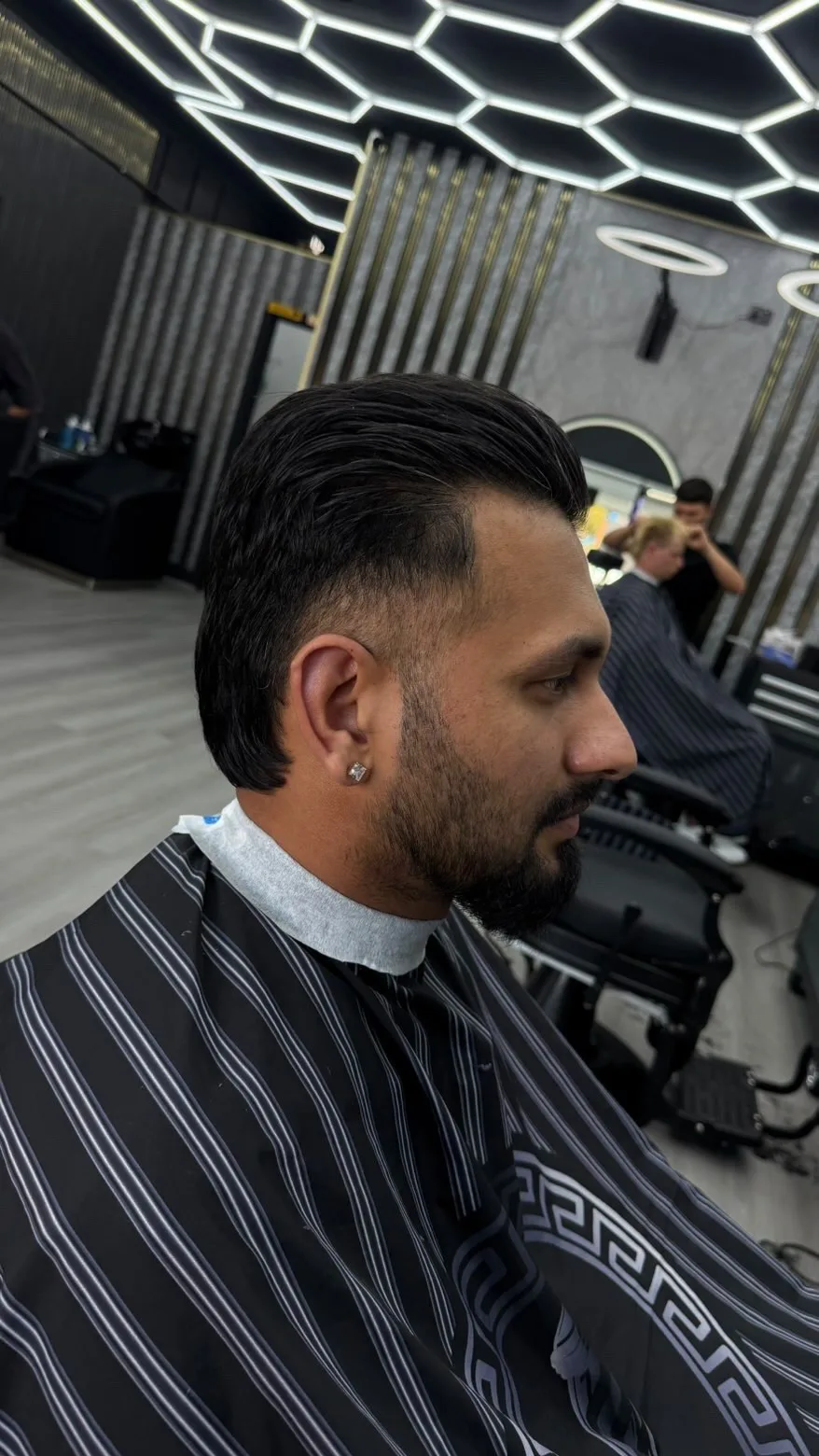 Side profile, slick top and skin fade, light beard line-up, striped cape.